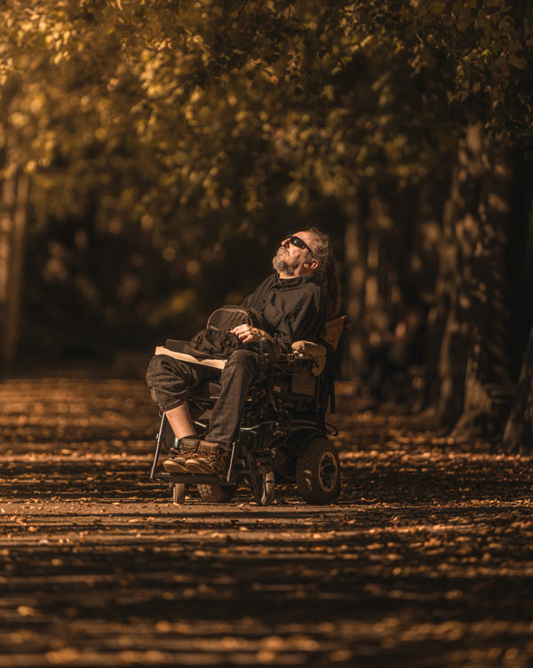 Photo: a white, bearded man in a wheelchair grieves while surrounded by trees.